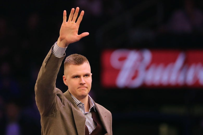 Porzingis, wearing a brown suit coat, waves to the crowd.